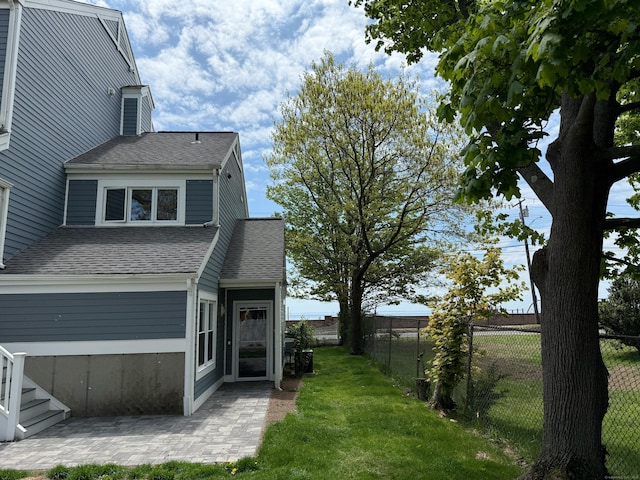 view of side of property with roof with shingles and a patio area