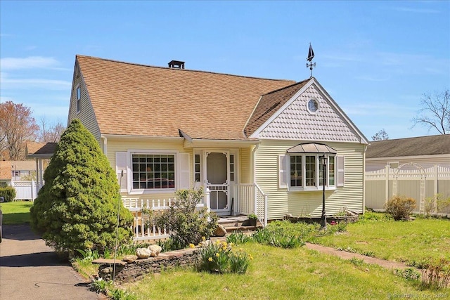 view of front of house featuring a shingled roof, fence, and a front yard