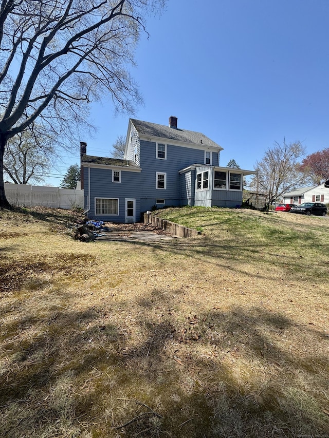 572 Forbes St, East Hartford, CT 06118 - back of house featuring fence, a lawn, a chimney, and a sunroom