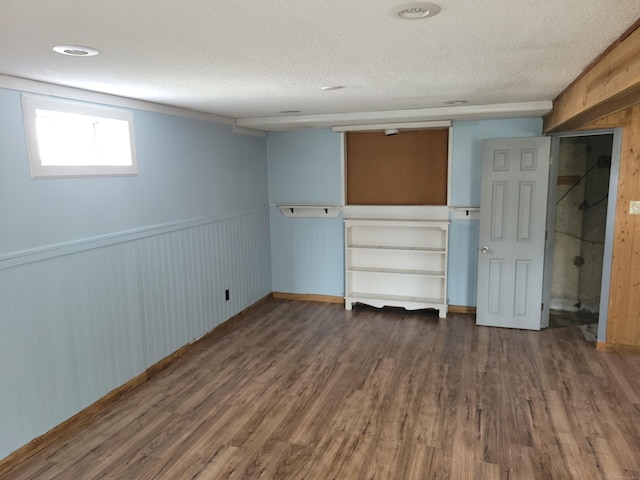 basement with a textured ceiling, wainscoting, wood finished floors, baseboards, and wooden walls