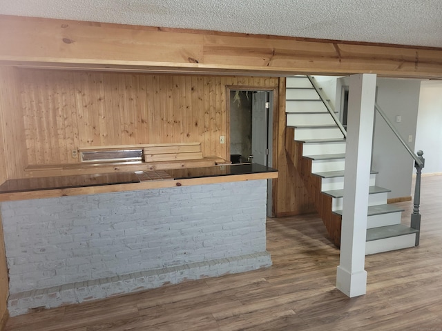 bar with a textured ceiling, wood finished floors, wooden walls, and stairway