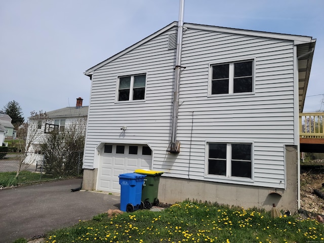 view of side of home featuring fence, an attached garage, and aphalt driveway