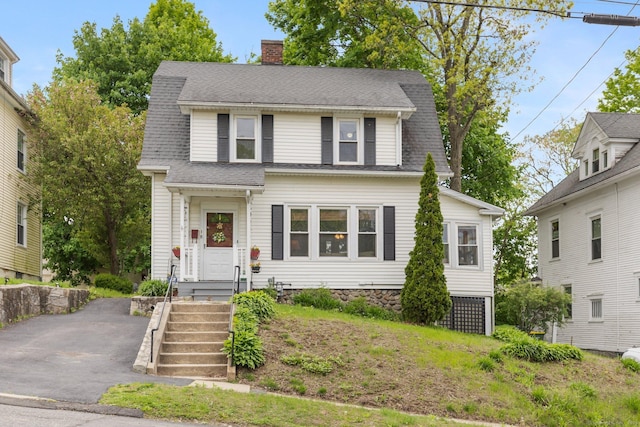 colonial inspired home featuring a chimney, driveway, and roof with shingles