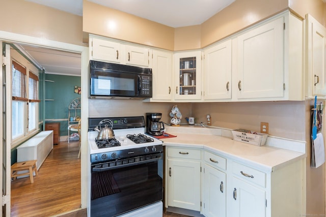 kitchen featuring gas range oven, black microwave, white cabinets, and light countertops