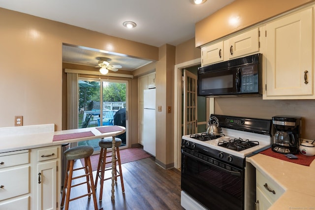 kitchen with gas range oven, black microwave, light countertops, dark wood-type flooring, and freestanding refrigerator