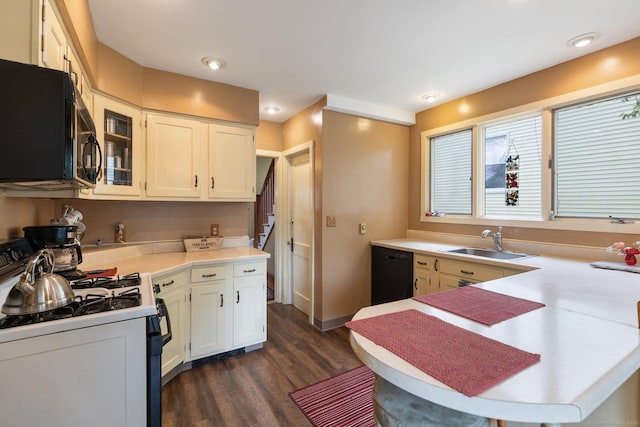 kitchen with black appliances, a sink, dark wood-type flooring, light countertops, and a peninsula