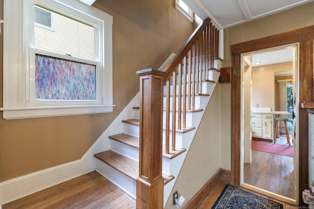 staircase featuring wood finished floors, plenty of natural light, and baseboards