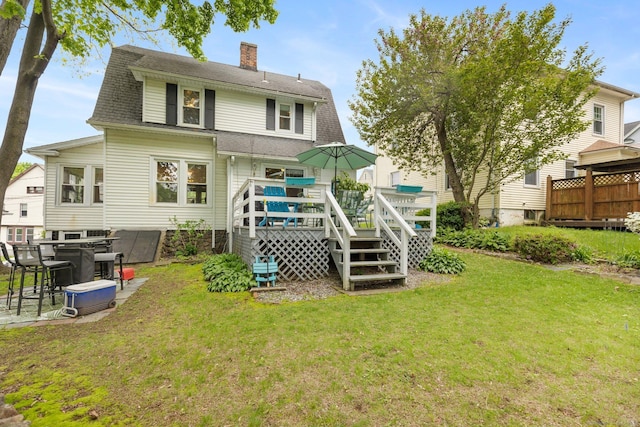 back of property featuring a chimney, a wooden deck, a lawn, and roof with shingles