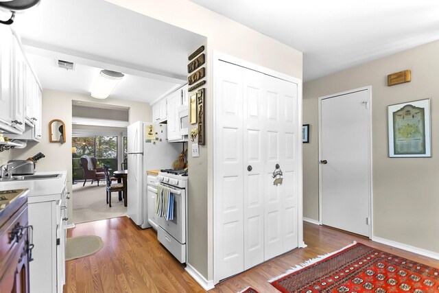 kitchen featuring white appliances, light wood finished floors, white cabinets, light countertops, and a sink