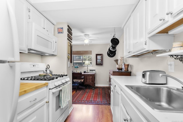 kitchen with white appliances, a sink, ceiling fan, white cabinetry, and wood finished floors