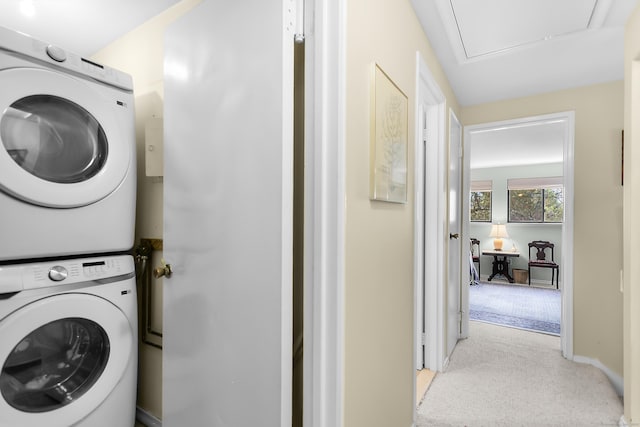 laundry area featuring stacked washing machine and dryer, light carpet, attic access, and baseboards