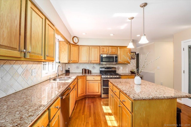 kitchen with light stone counters, appliances with stainless steel finishes, a sink, and light wood-type flooring