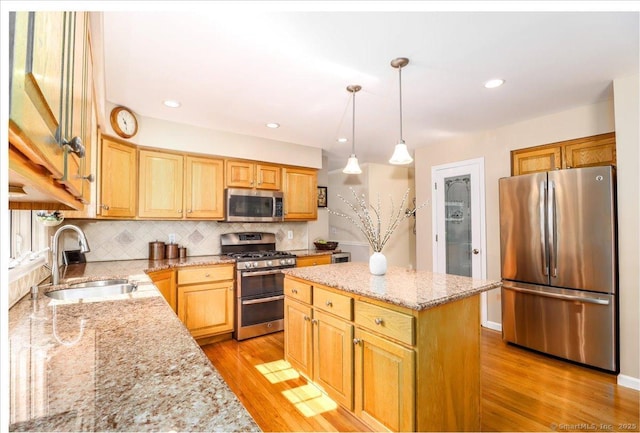 kitchen featuring appliances with stainless steel finishes, light stone counters, a sink, a center island, and backsplash