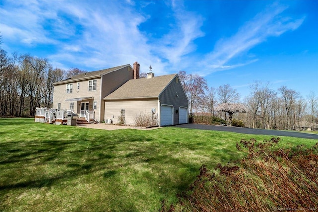 rear view of property with a chimney, a wooden deck, a garage, aphalt driveway, and a yard