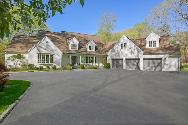 cape cod house with driveway, a porch, and a garage