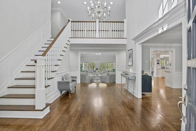 entryway with a chandelier, a decorative wall, stairway, ornamental molding, and dark wood-style floors