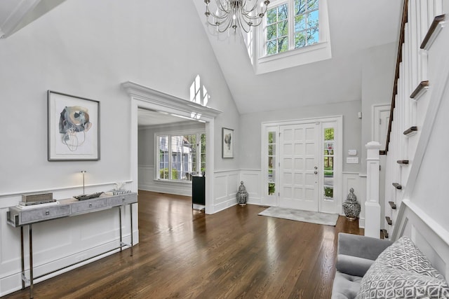 entryway featuring high vaulted ceiling, healthy amount of natural light, a chandelier, a decorative wall, and wood finished floors