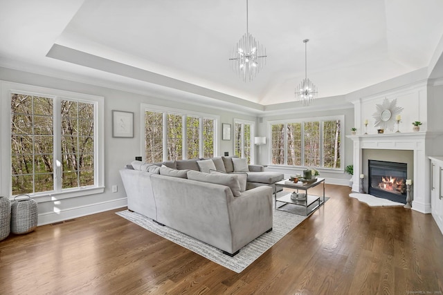 living area featuring a tray ceiling, a chandelier, healthy amount of natural light, and a glass covered fireplace