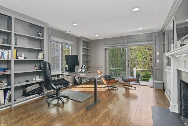 home office featuring a decorative wall, ornamental molding, wood finished floors, a fireplace with flush hearth, and recessed lighting