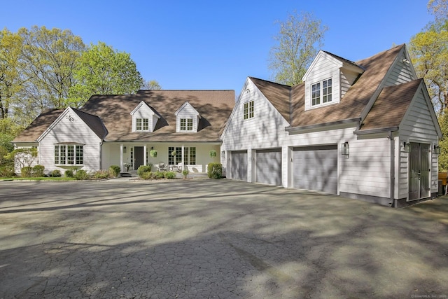 new england style home featuring a porch, driveway, and a shingled roof