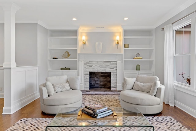 living area featuring wood finished floors, ornamental molding, ornate columns, built in shelves, and baseboards