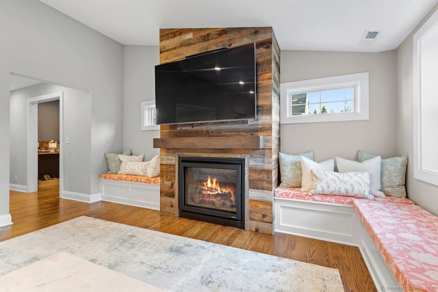 living area with lofted ceiling, baseboards, visible vents, wood finished floors, and a large fireplace
