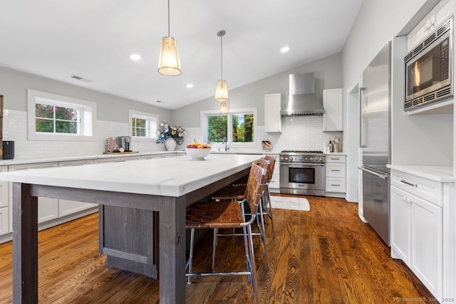 kitchen featuring wall chimney exhaust hood, premium appliances, visible vents, decorative backsplash, and vaulted ceiling