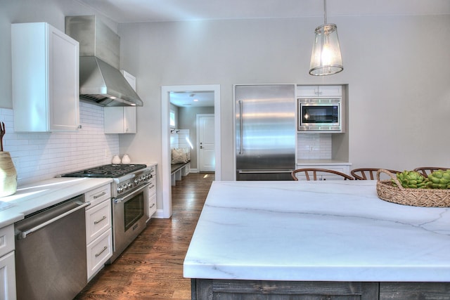 kitchen featuring built in appliances, tasteful backsplash, dark wood-type flooring, wall chimney exhaust hood, and white cabinets
