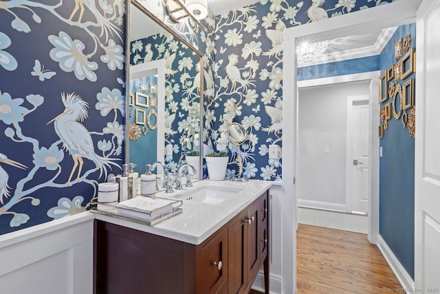 bathroom featuring vanity, baseboards, wallpapered walls, and wood finished floors