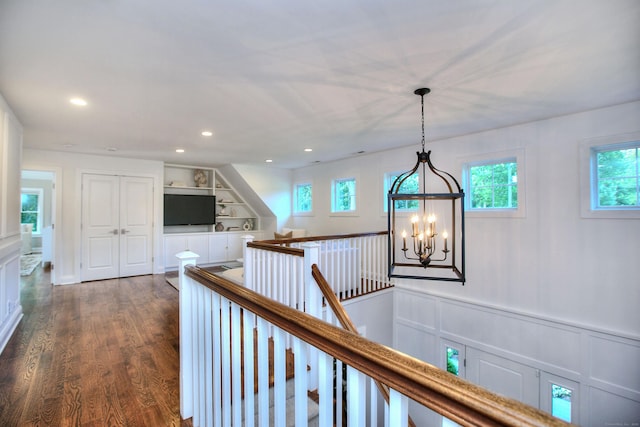 hall featuring dark wood-style flooring, a wealth of natural light, a decorative wall, and an upstairs landing
