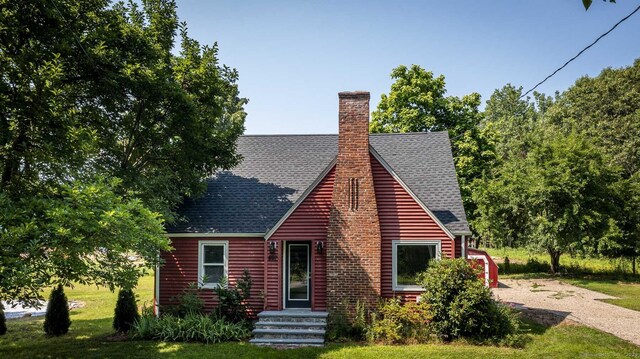 view of front of home featuring a chimney, a shingled roof, and a front yard