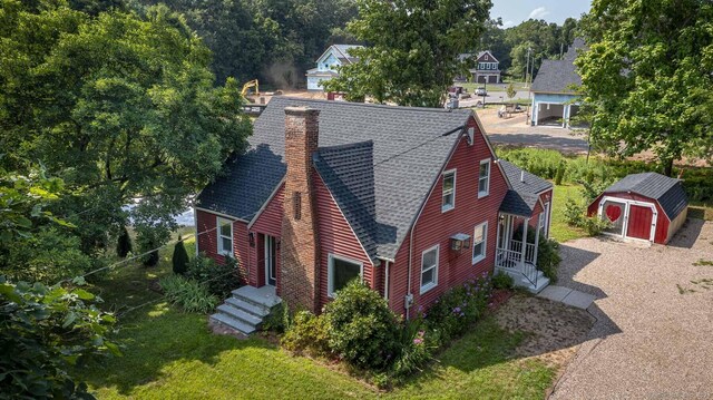 exterior space with a storage shed, an outdoor structure, a shingled roof, and a chimney