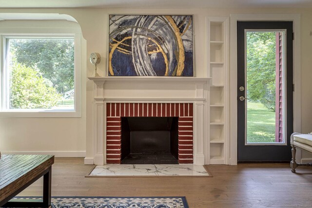 interior details with baseboards, built in features, a brick fireplace, and wood finished floors