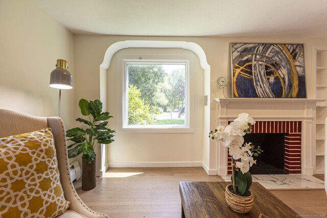 living area with baseboards, a brick fireplace, and wood finished floors