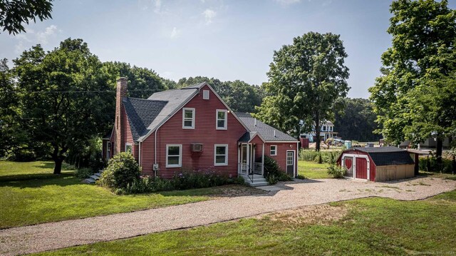 view of front of house featuring a storage unit, an outbuilding, a shingled roof, and a front lawn