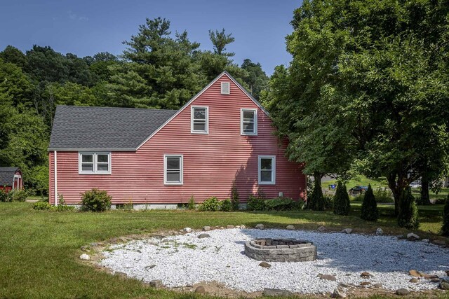back of property featuring roof with shingles, a lawn, and an outdoor fire pit