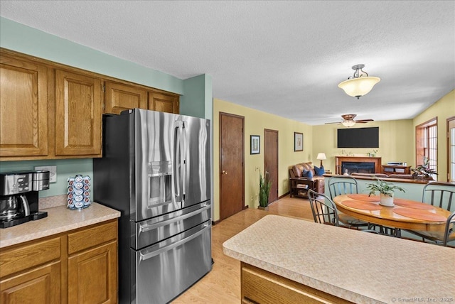 kitchen with light wood-style floors, brown cabinets, a fireplace, and stainless steel refrigerator with ice dispenser