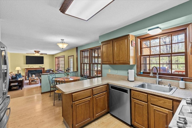 kitchen with a sink, stainless steel dishwasher, a peninsula, and brown cabinetry