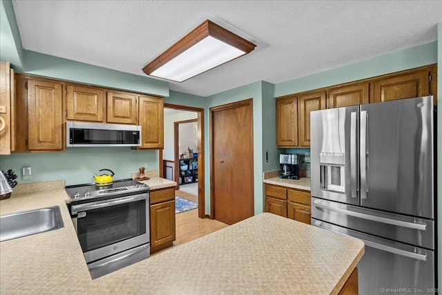 kitchen featuring a sink, light countertops, a textured ceiling, brown cabinetry, and stainless steel appliances
