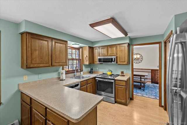 kitchen featuring brown cabinetry, light wood-style floors, a textured ceiling, a sink, and appliances with stainless steel finishes