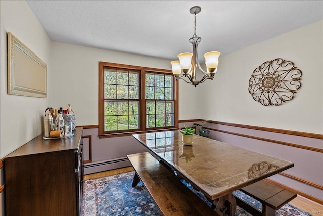 dining space featuring an inviting chandelier, a baseboard radiator, a textured ceiling, and wood finished floors