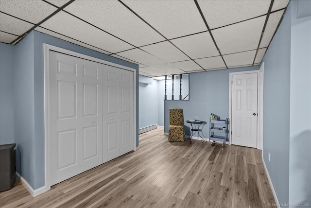 finished basement with baseboards, a paneled ceiling, light wood-style flooring, and a baseboard radiator
