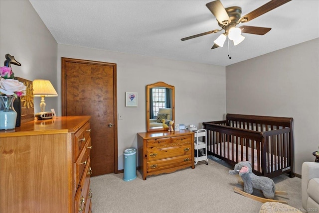 bedroom featuring a crib, light carpet, and a ceiling fan