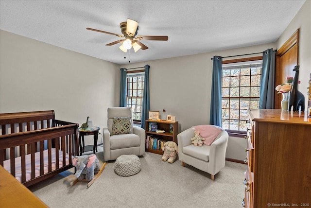bedroom with a ceiling fan, baseboards, a textured ceiling, a crib, and carpet flooring