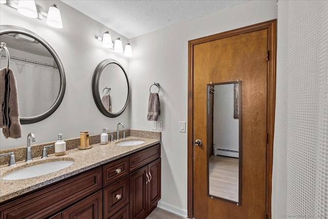 bathroom featuring double vanity, a textured ceiling, a baseboard heating unit, and a sink