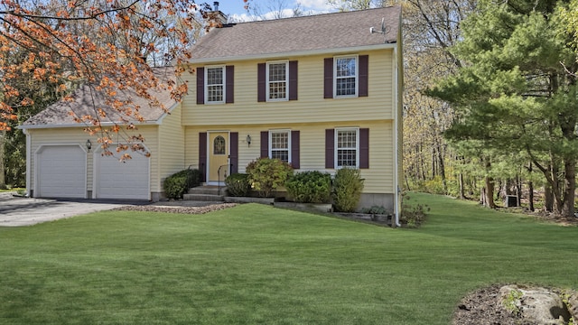 colonial house featuring roof with shingles, a front lawn, aphalt driveway, a garage, and a chimney