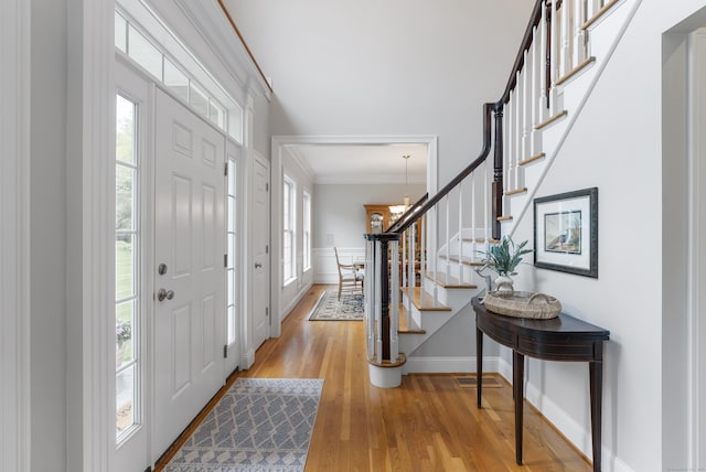 foyer featuring baseboards, light wood finished floors, visible vents, crown molding, and stairway