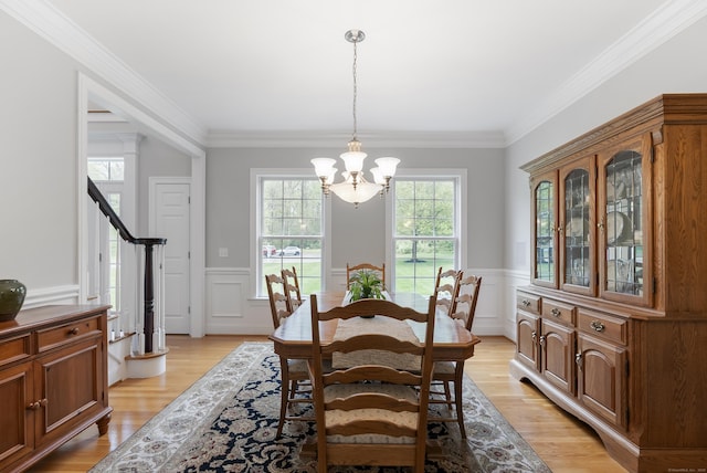 dining space with wainscoting, ornamental molding, a notable chandelier, and light wood-style floors