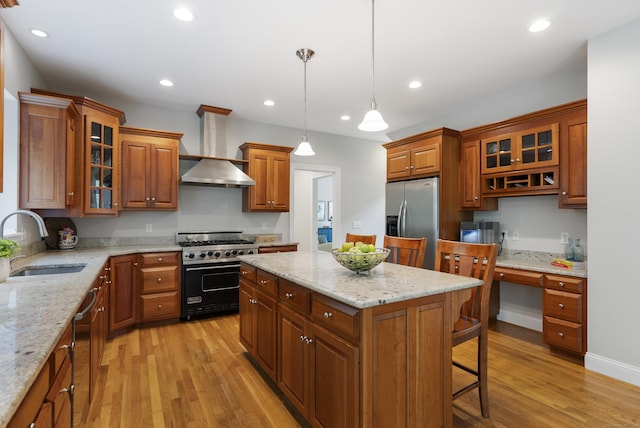 kitchen with brown cabinetry, a breakfast bar, a sink, wall chimney range hood, and stainless steel appliances