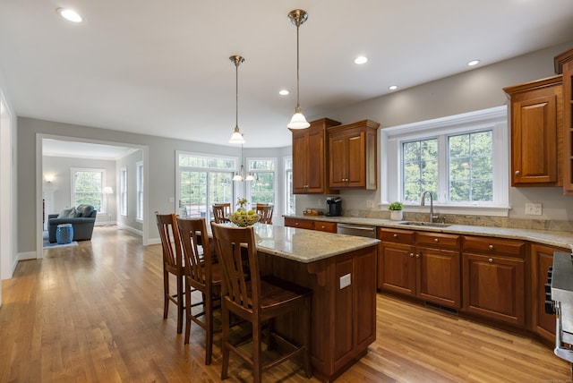 kitchen with a sink, brown cabinetry, a breakfast bar, light wood finished floors, and light stone countertops